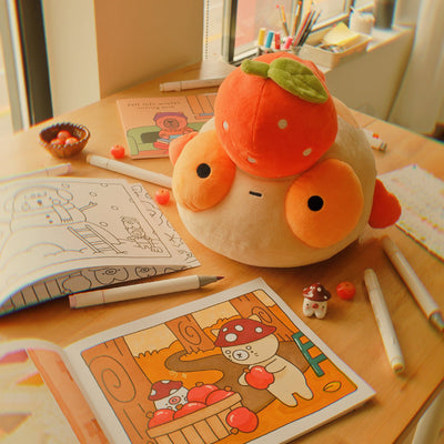 Plush Tangerine Maxine on a table with the Fall into Winter coloring book and art supplies.